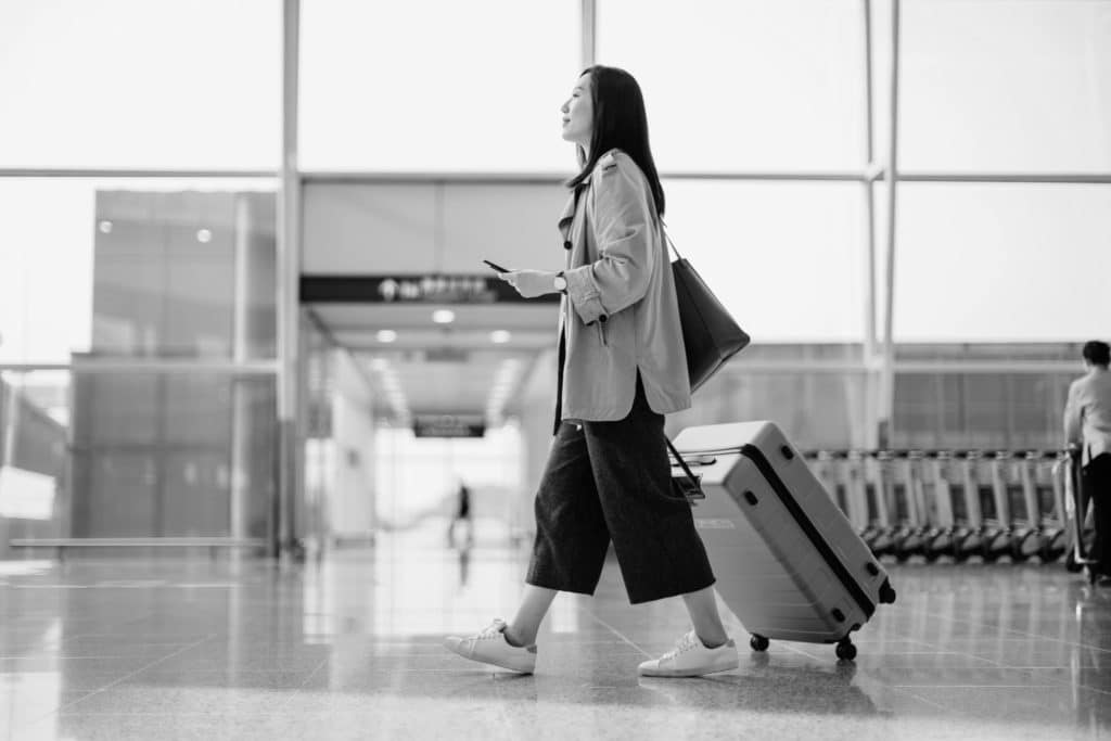 Frau am Flughafen zieht Koffer hinter sich her.
